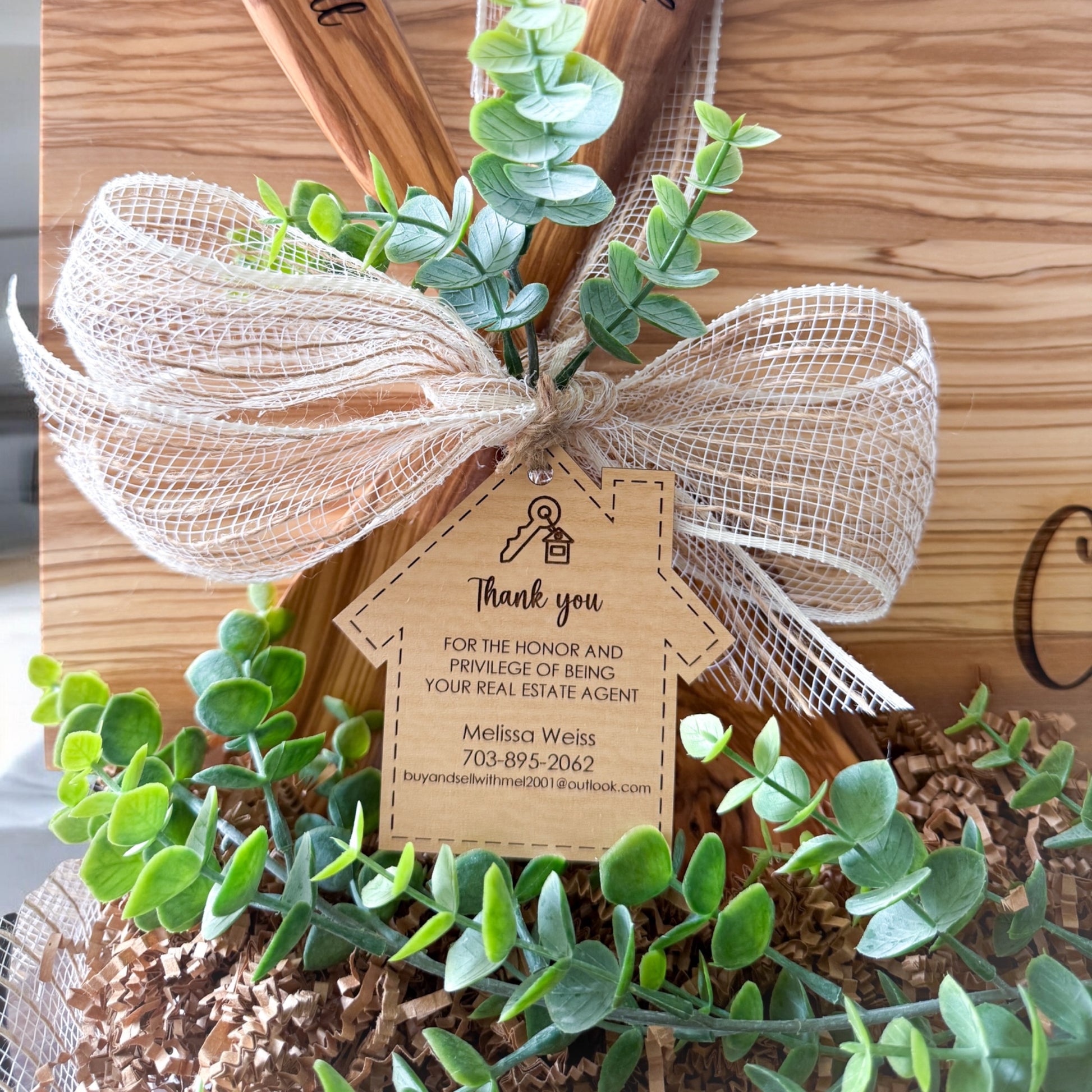 Close-up of personalized realtor thank you tag attached to luxury olive wood closing gift basket with greenery and ribbon, custom real estate client appreciation gift for home buyers, closing day gifts, and memorable housewarming presents.