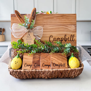 Luxury personalized olive wood realtor closing gift basket featuring engraved cutting board, custom coasters, olive wood serving spoons, greenery, and house-shaped thank you tag for home buyers, housewarming gifts, and real estate client appreciation gifts.