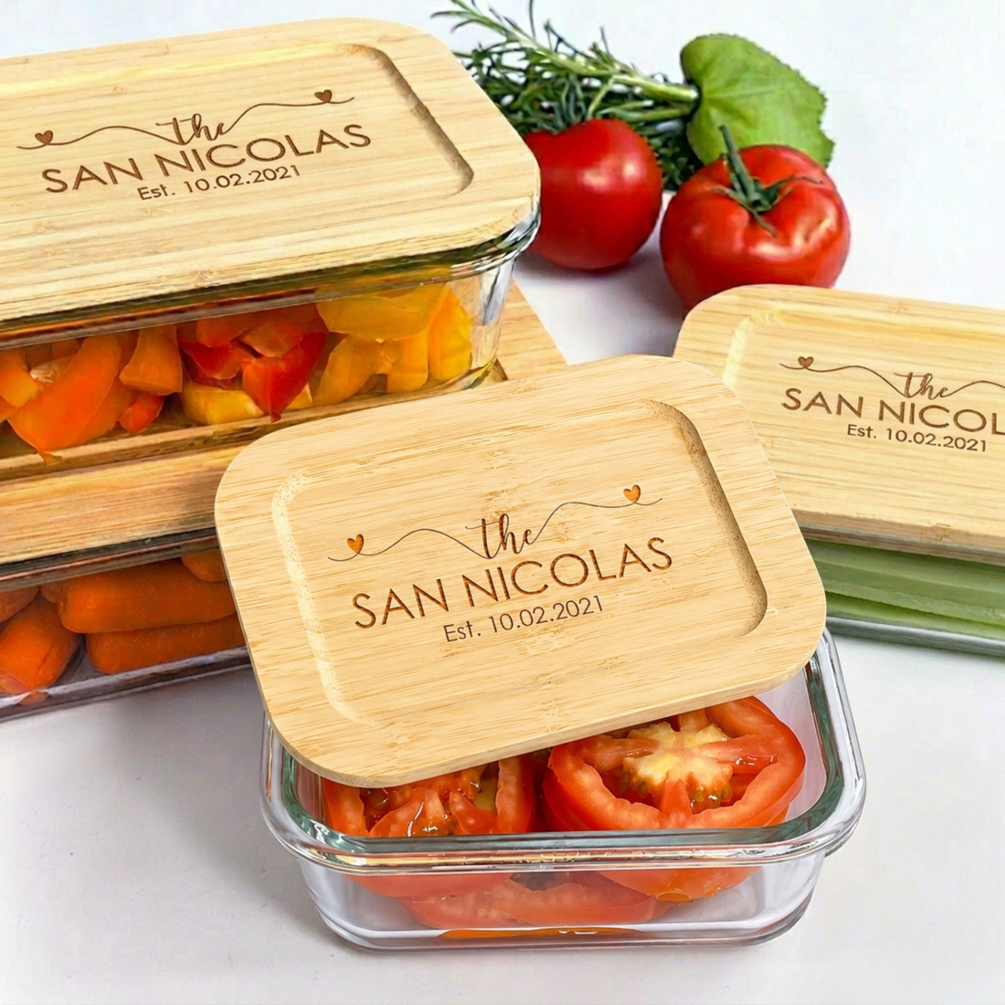 Personalized glass food storage container set with engraved bamboo lids featuring custom family name and established date. Elegant reusable kitchen storage containers styled with fresh vegetables and tomatoes for luxury realtor closing gifts, personalized housewarming gifts, and modern kitchen organization.
