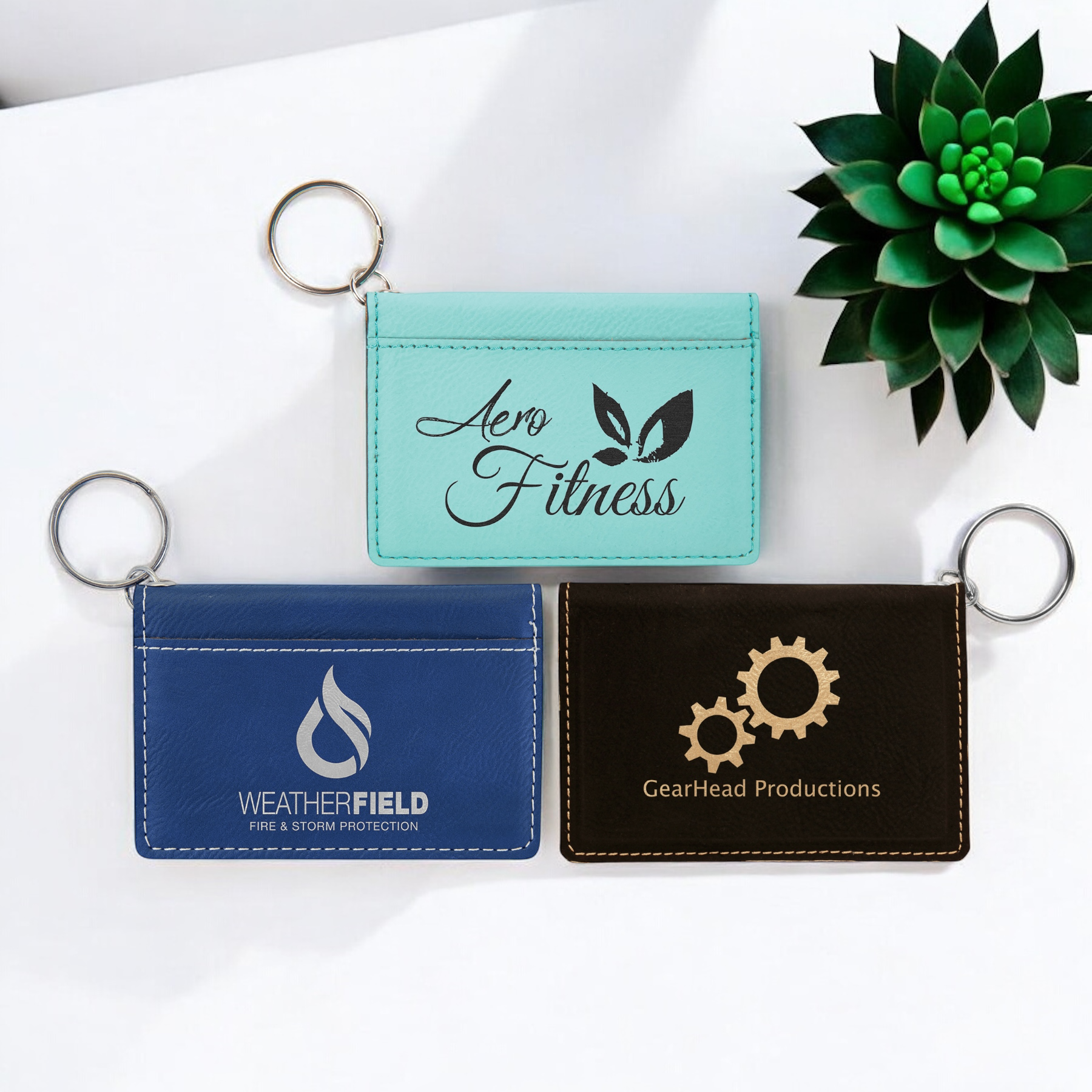 Custom laser-engraved leatherette keychain ID holders in teal, blue, and black, featuring snap closure, exterior pocket, and silver key ring for corporate branding, employee gifts, promotional producuts or personalized gifts.