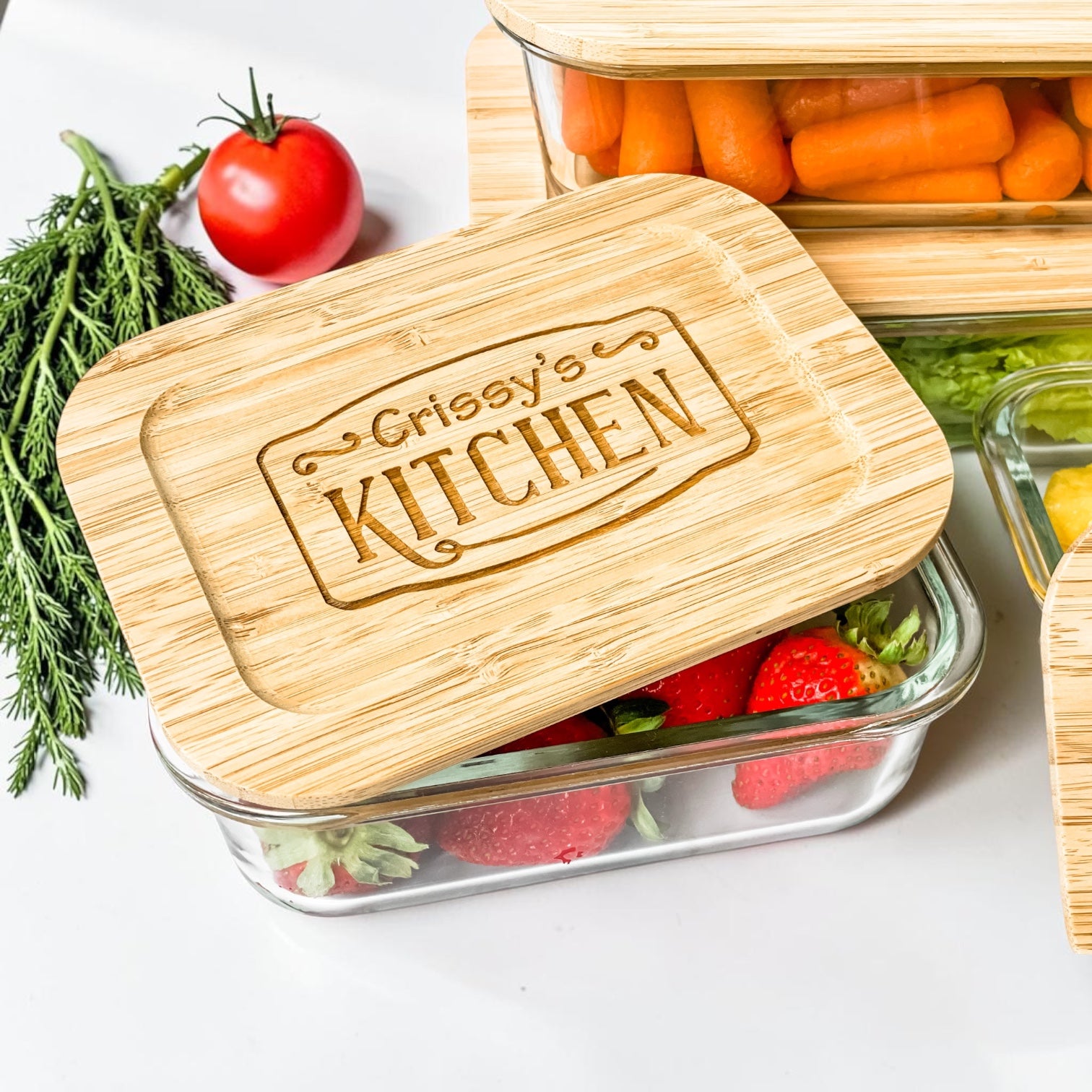 Close-up of a luxury personalized glass food storage container with engraved bamboo lid displayed with fresh strawberries and vegetables. Elegant realtor closing gift and custom housewarming gift designed for sustainable kitchen organization, elevated everyday living, meal prep, and modern homeowner gifting.