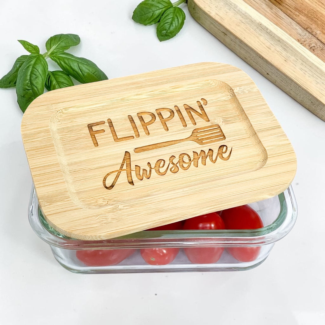 Set of engraved glass food storage containers with humorous kitchen pun bamboo lids including “Flippin’ Awesome,” “Just Roll With It,” and “Cut It Out.” Reusable eco-friendly kitchen containers styled with fresh produce, ideal for realtor closing gifts, client appreciation gifts, and personalized housewarming presents.