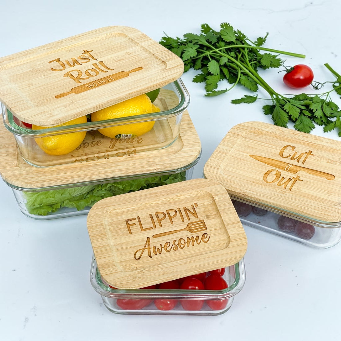 Set of engraved glass food storage containers with humorous kitchen pun bamboo lids including “Flippin’ Awesome,” “Just Roll With It,” and “Cut It Out.” Reusable eco-friendly kitchen containers styled with fresh produce, ideal for realtor closing gifts, client appreciation gifts, and personalized housewarming presents.