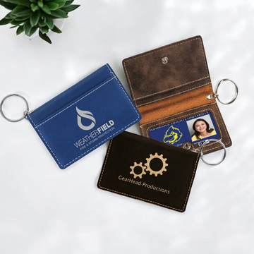 Custom laser-engraved leatherette keychain ID holder with snap closure, exterior pocket, interior card slots, clear ID window, and silver key ring for corporate branding or personalized gifts.