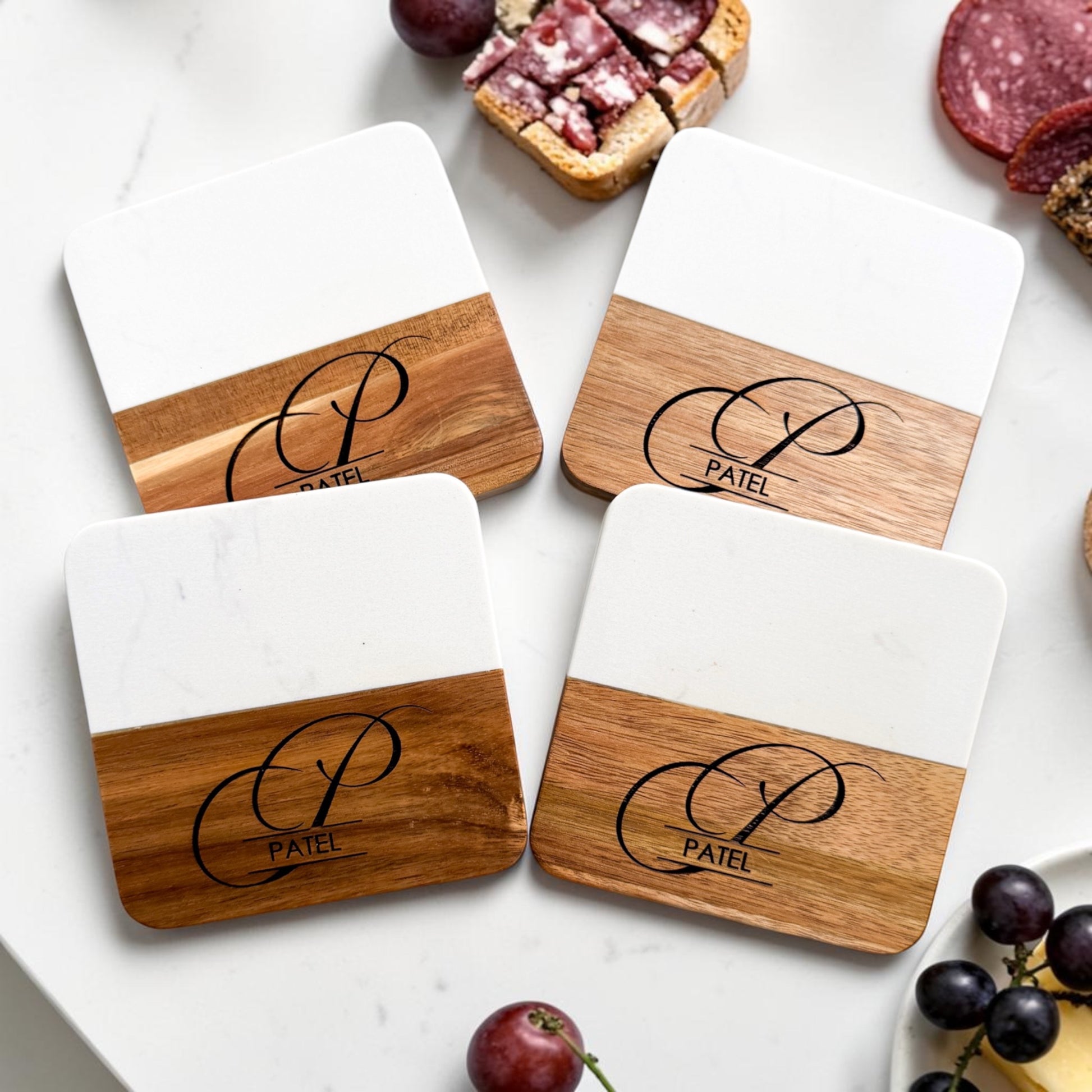 Luxury marble and acacia wood personalized coaster set engraved with monogram and family name styled with charcuterie and grapes for modern housewarming gifts and realtor client gifting