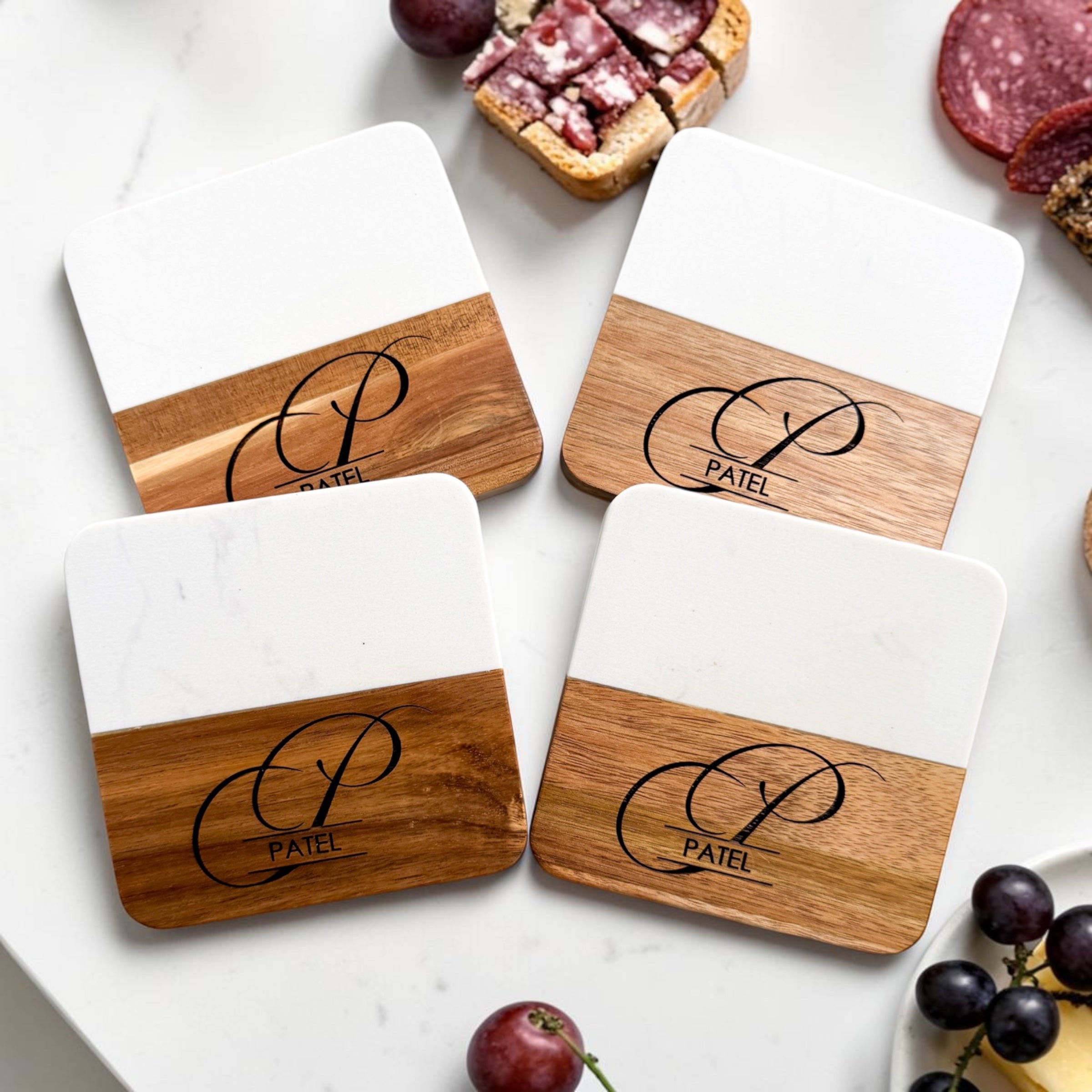 Luxury marble and acacia wood personalized coaster set engraved with monogram and family name styled with charcuterie and grapes for modern housewarming gifts and realtor client gifting
