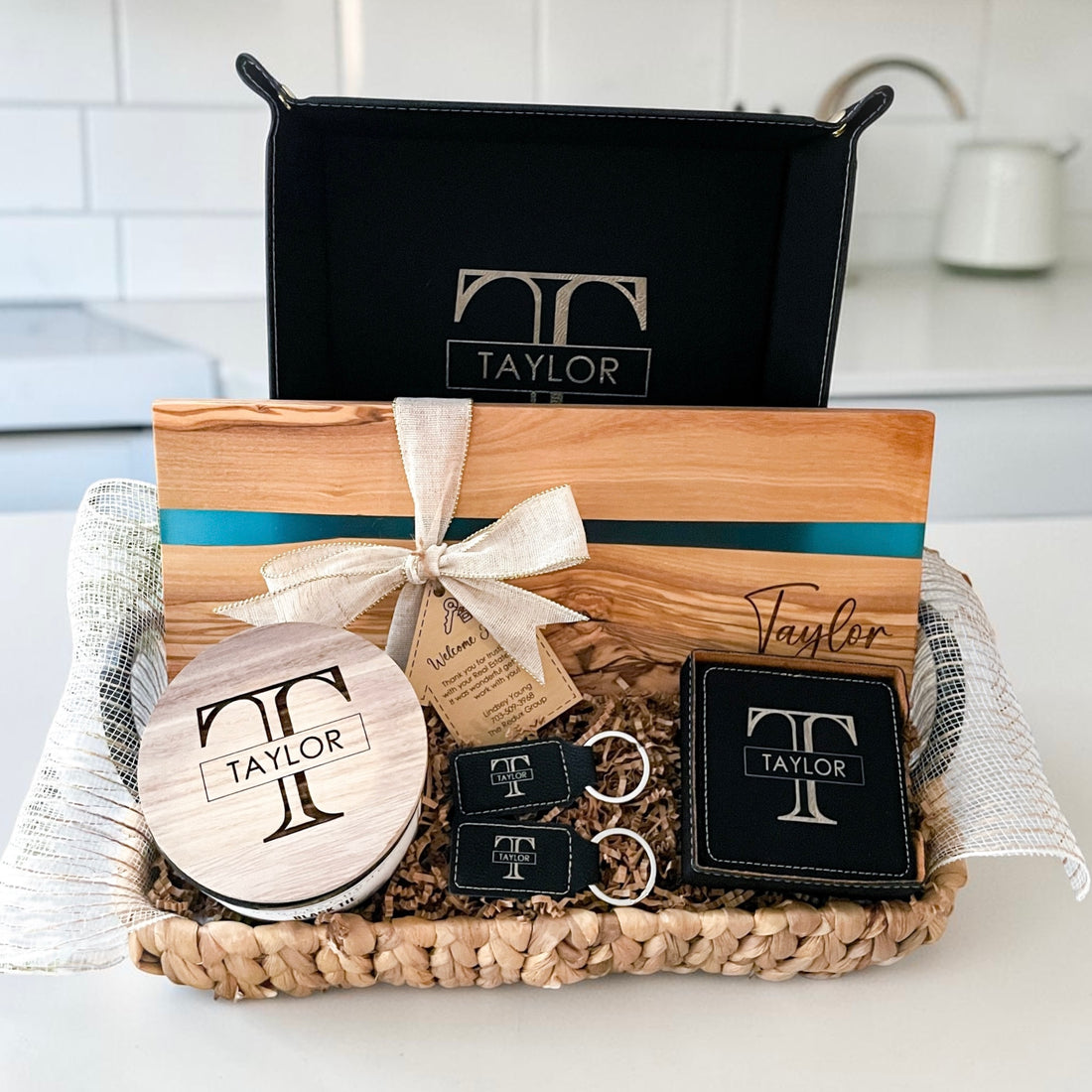Luxury personalized closing gift basket with blue resin olive wood serving board, engraved leatherette coasters, keychains, candle, and vanity tray designed for realtor closing gifts and upscale housewarming presents