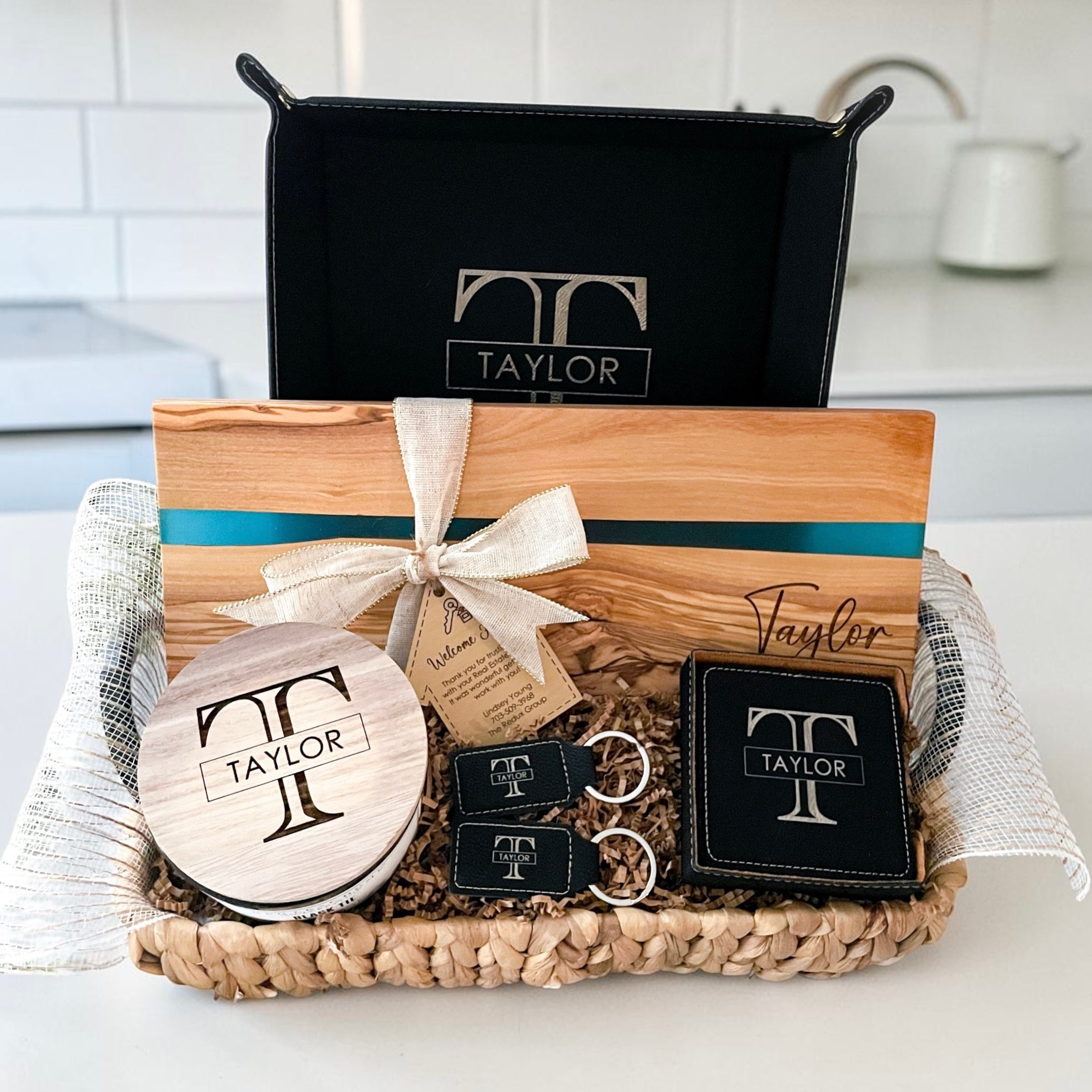 Luxury personalized closing gift basket with blue resin olive wood serving board, engraved leatherette coasters, keychains, candle, and vanity tray designed for realtor closing gifts and upscale housewarming presents