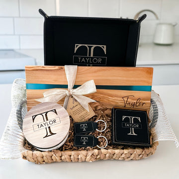 Luxury personalized closing gift basket with blue resin olive wood serving board, engraved leatherette coasters, keychains, candle, and vanity tray designed for realtor closing gifts and upscale housewarming presents