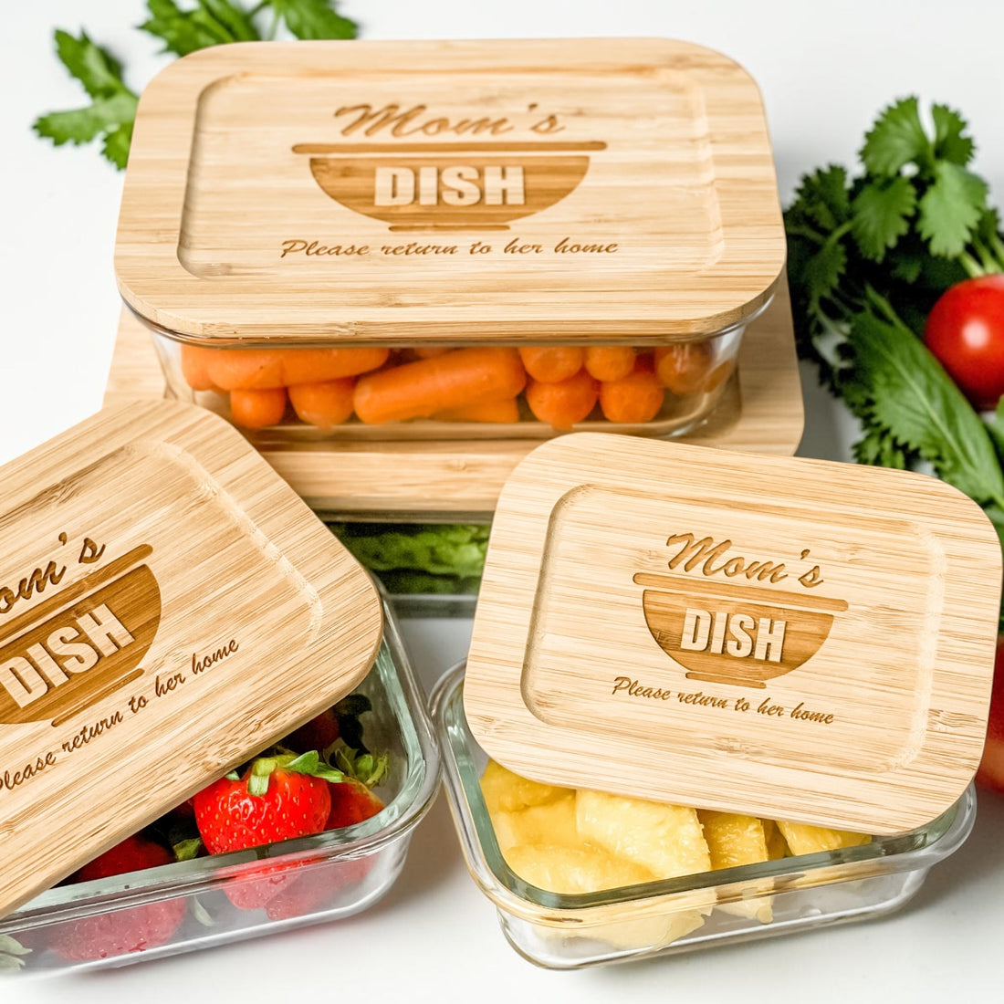 Personalized glass food storage container set with engraved bamboo lids featuring “Mom’s Dish – Please Return to Her Home” design. Elegant reusable kitchen storage containers styled with fresh fruit and vegetables, perfect for thoughtful realtor closing gifts, housewarming gifts, and custom kitchen décor.