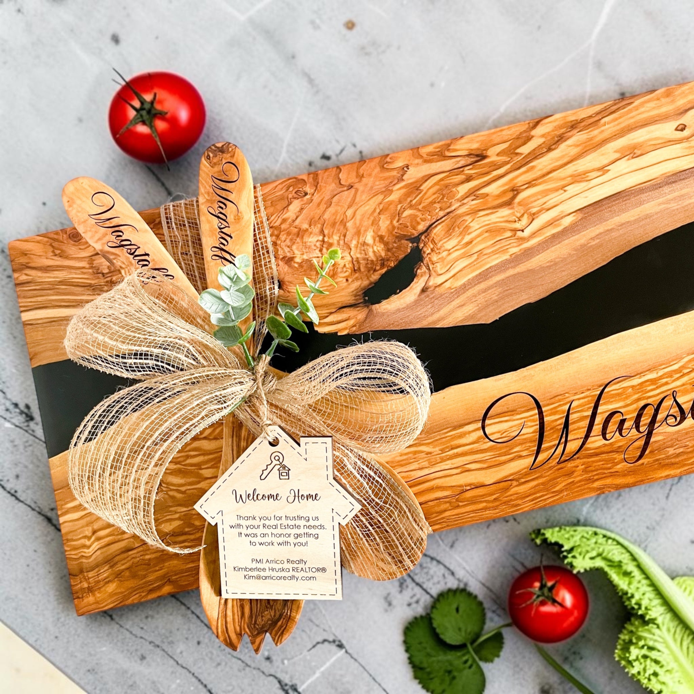 Luxury realtor closing gift featuring personalized olive wood and black resin cutting board with engraved serving utensils, welcome home gift tag, and kitchen styling for home buyers