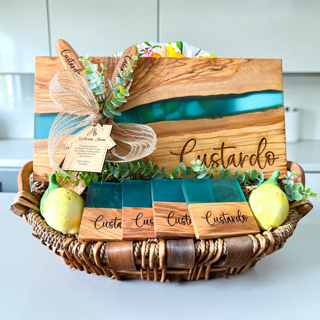 Luxury personalized blue river resin and olive wood cutting board gift basket with engraved coasters, wooden serving spoons, and custom welcome home gift tag designed for realtor closing gifts and upscale housewarming celebrations