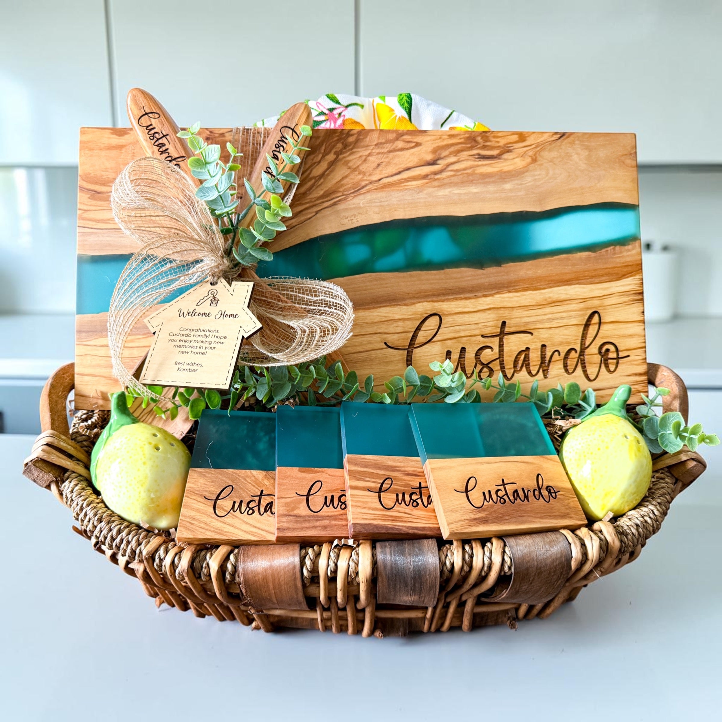Luxury personalized blue river resin and olive wood cutting board gift basket with engraved coasters, wooden serving spoons, and custom welcome home gift tag designed for realtor closing gifts and upscale housewarming celebrations