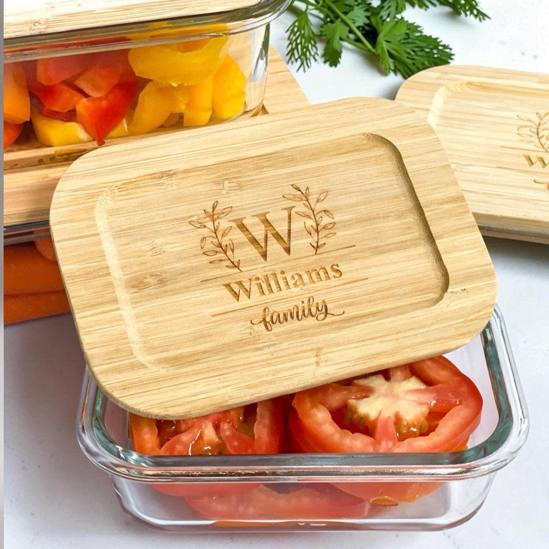 Personalized glass food storage container set with engraved bamboo lids displayed with fresh vegetables. Elegant realtor closing gift and luxury housewarming gift idea for new homeowners, kitchen organization, meal prep, sustainable food storage, and personalized client appreciation gifts.