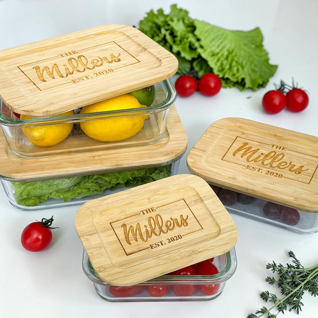 Luxury personalized glass food storage container set with engraved bamboo lids featuring custom family name and established date. Elegant reusable kitchen organization containers styled with fresh produce, lemons, lettuce, and tomatoes for realtor closing gifts, housewarming gifts, and modern kitchen décor.