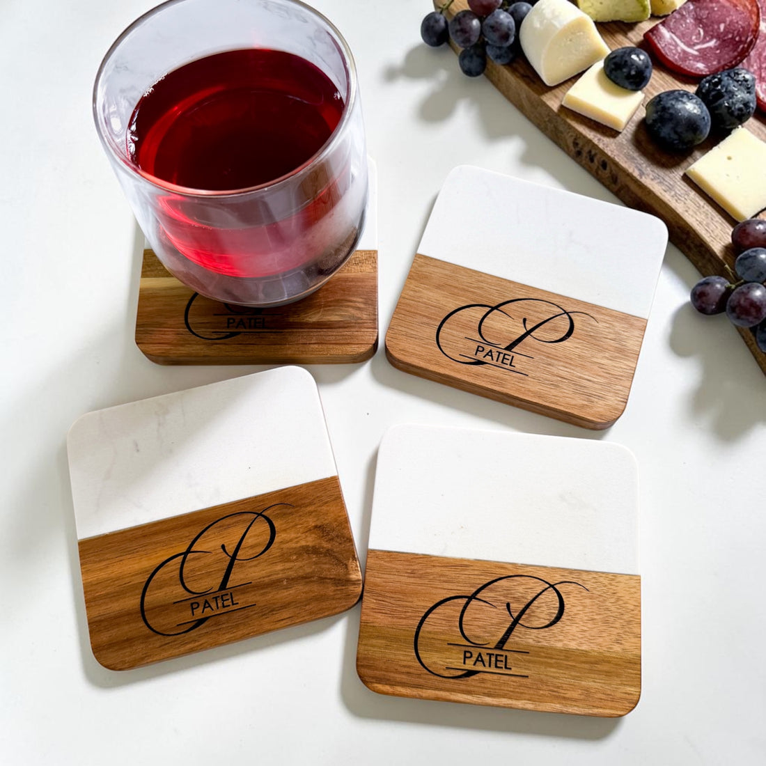 Personalized marble and acacia wood coaster set engraved with monogram and family name styled with wine glass and charcuterie board as a luxury realtor closing gift and housewarming gift