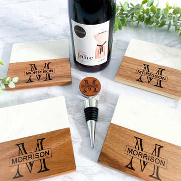 Personalized marble and acacia wood coaster set with engraved monogram and matching wine stopper displayed with a wine bottle on a marble countertop. Elegant custom housewarming gift, wedding gift, realtor closing gift, and anniversary gift for wine lovers and new homeowners.