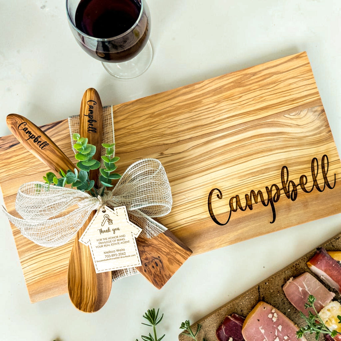 Luxury personalized olive wood realtor closing gift basket featuring engraved cutting board, custom coasters, olive wood serving spoons, greenery, and house-shaped thank you tag for home buyers, housewarming gifts, and real estate client appreciation gifts.