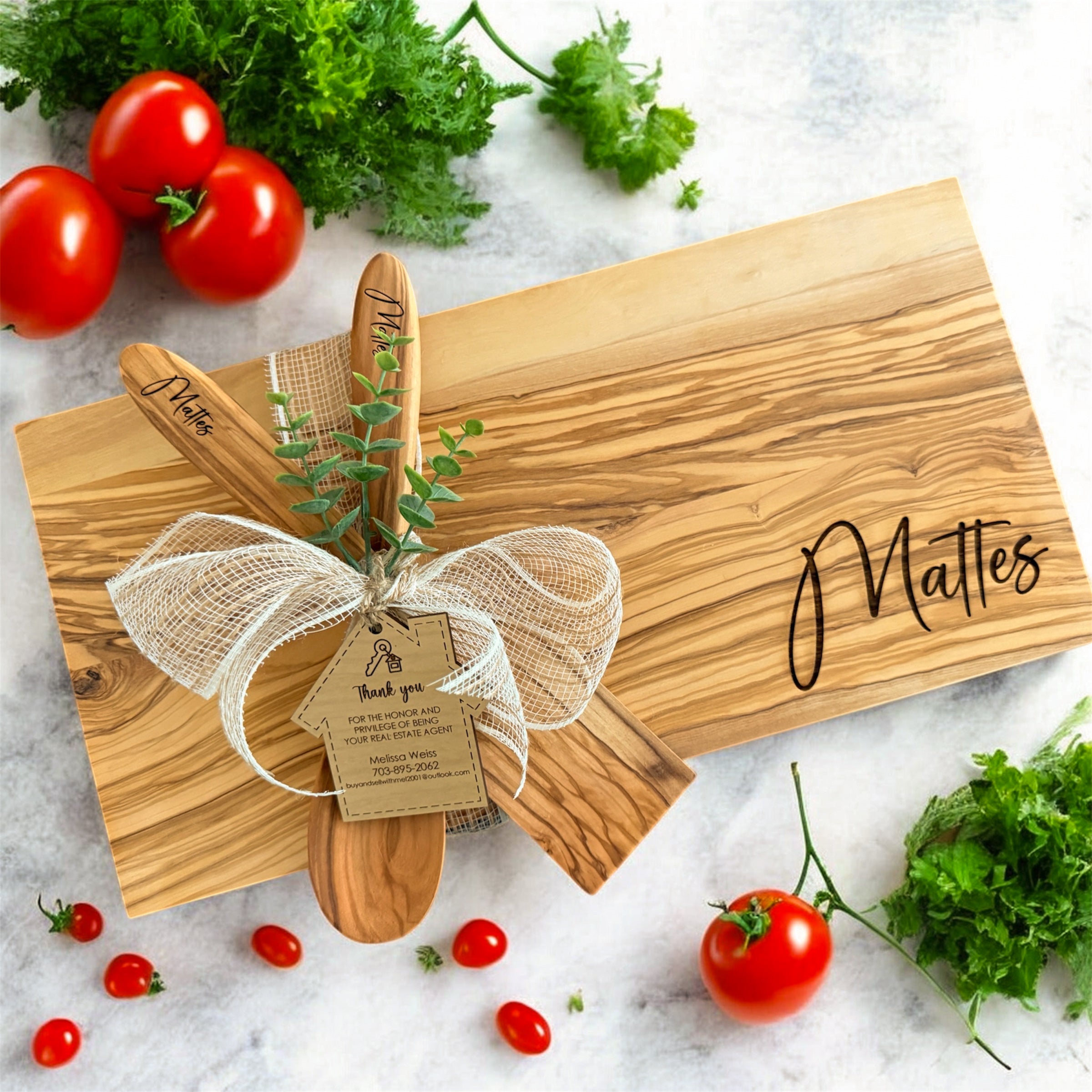 Luxury personalized olive wood cutting board with engraved family name, matching wooden serving utensils, and custom realtor gift tag styled as an upscale housewarming and closing gift